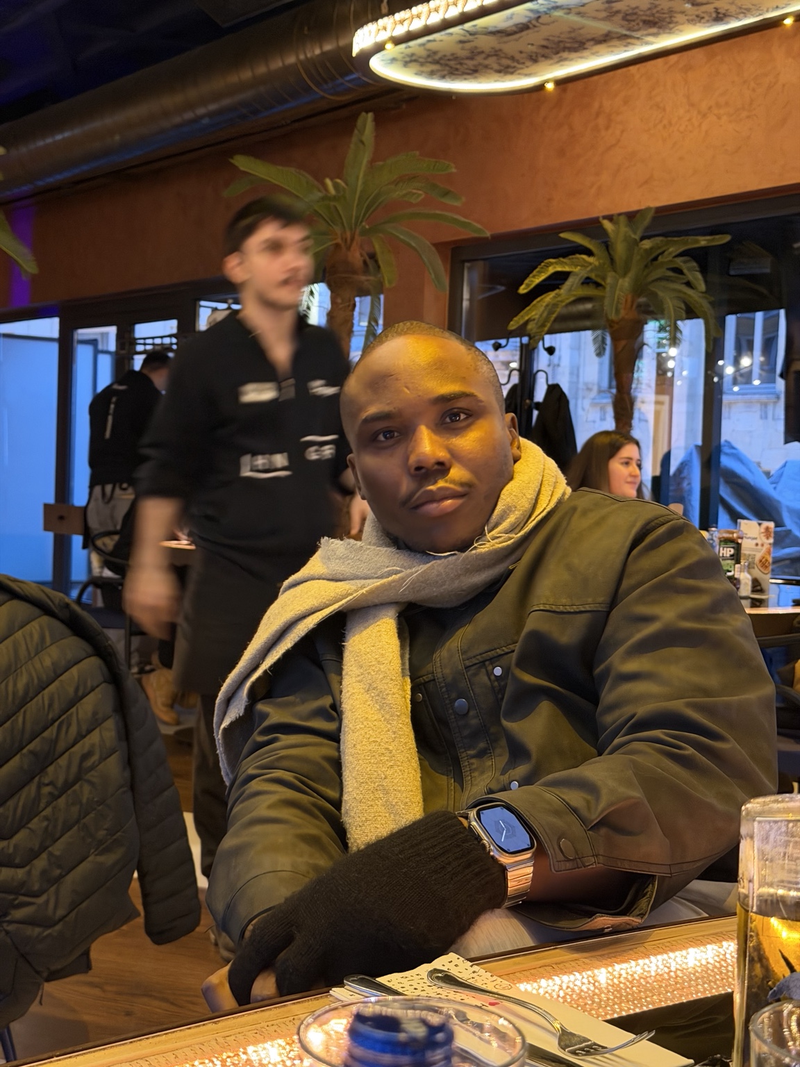 Ekulide Miracle seated at a restaurant, wearing a dark jacket and scarf