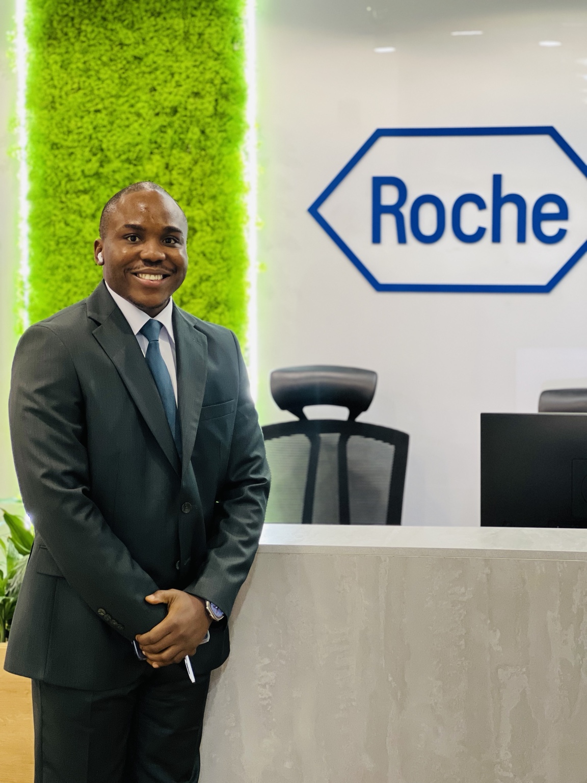 Ekulide Miracle standing in a suit at the Roche workplace reception