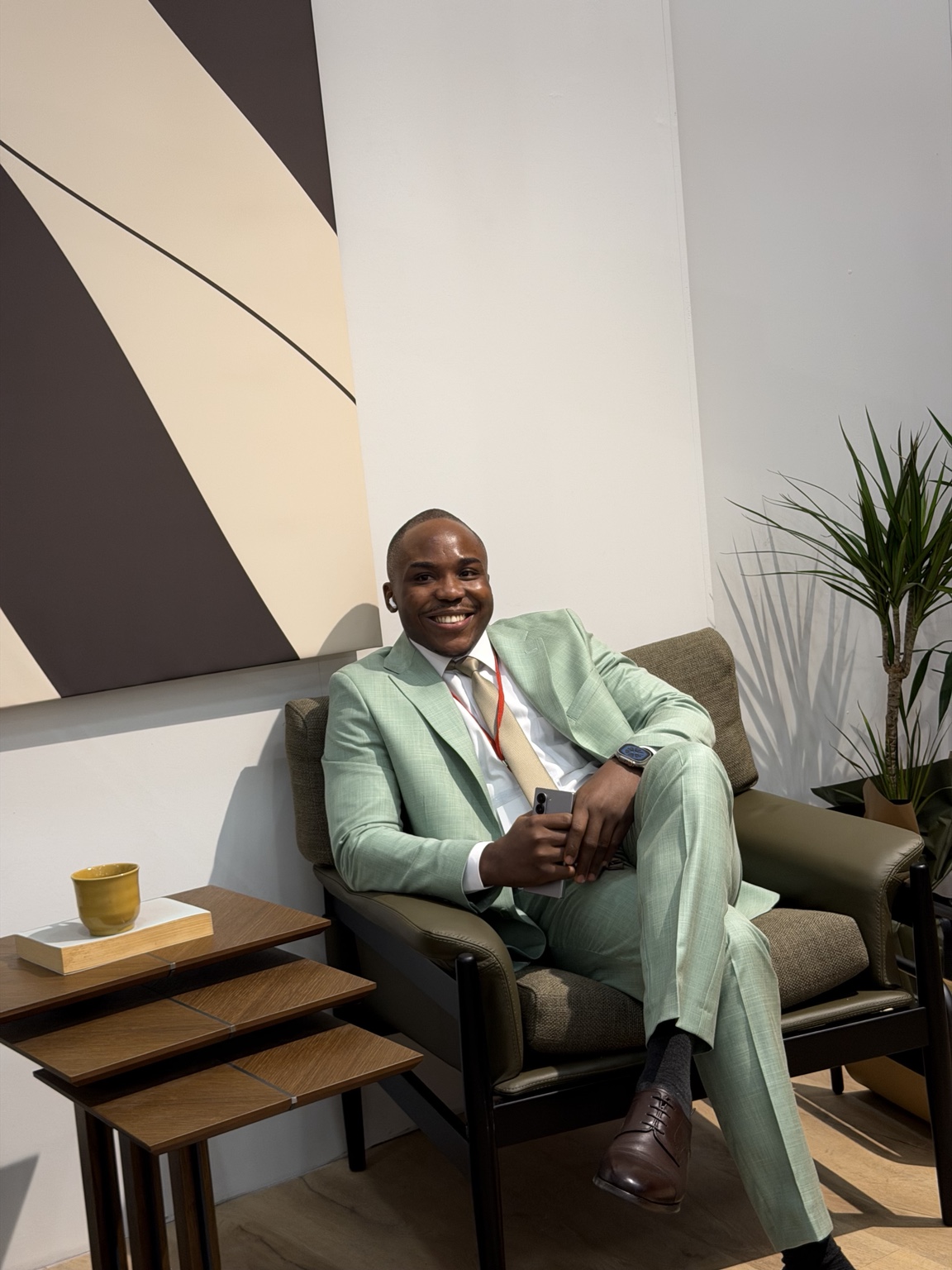 Ekulide Miracle seated in a mint-green suit, with the surrounding interior in view