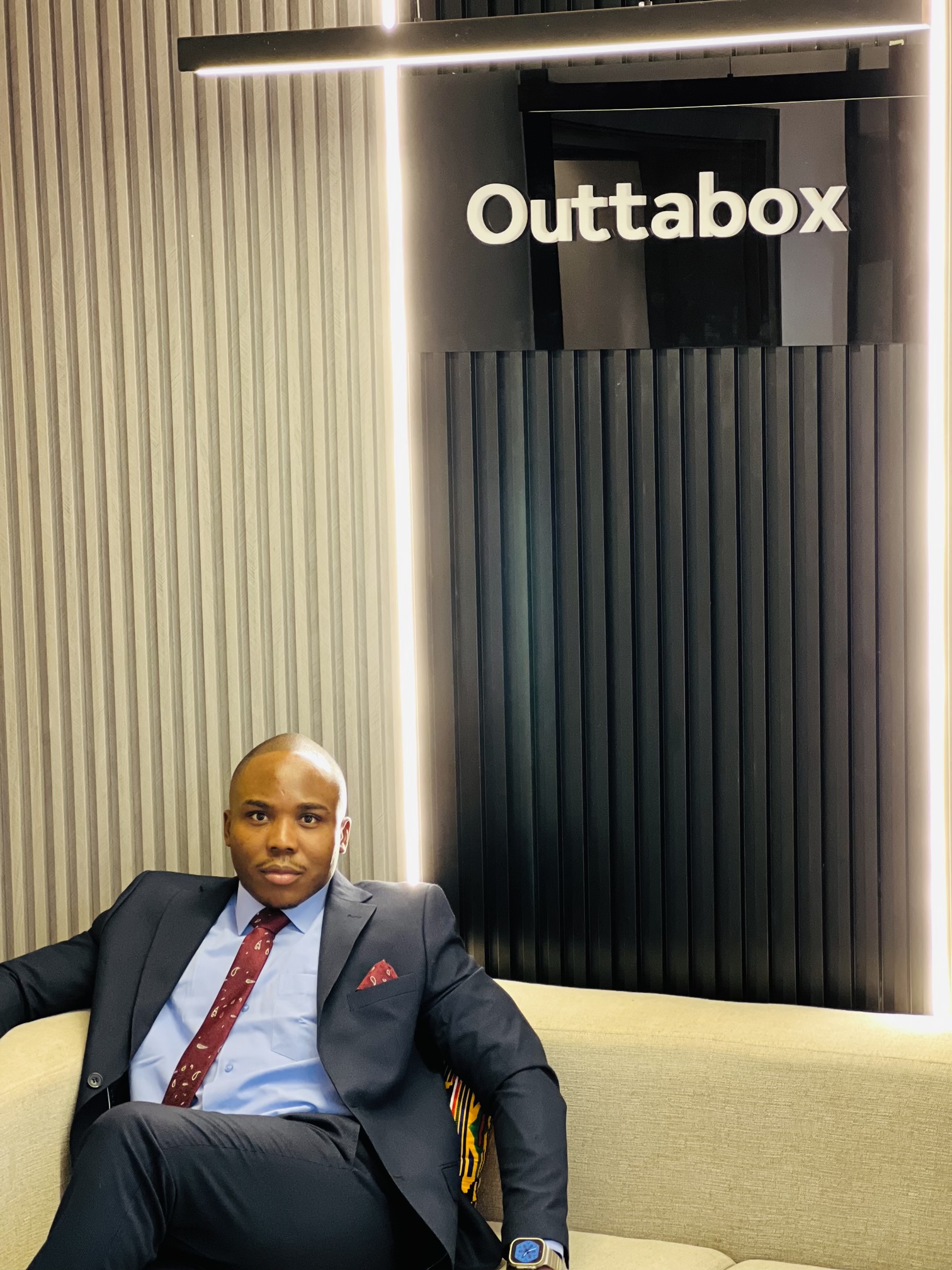 Ekulide Miracle seated in the Outtabox office beneath the company wordmark